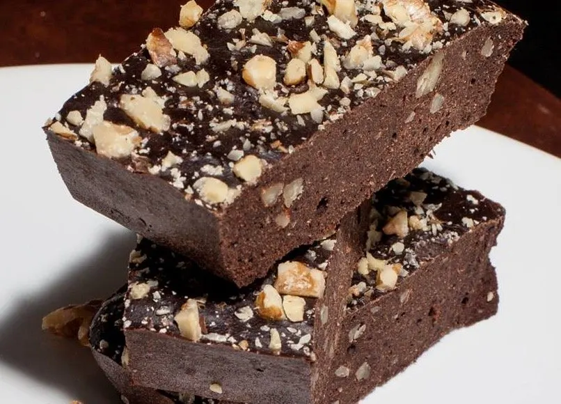 Dos barras de proteína de chocolate con nueces picadas por encima, apiladas en un plato blanco