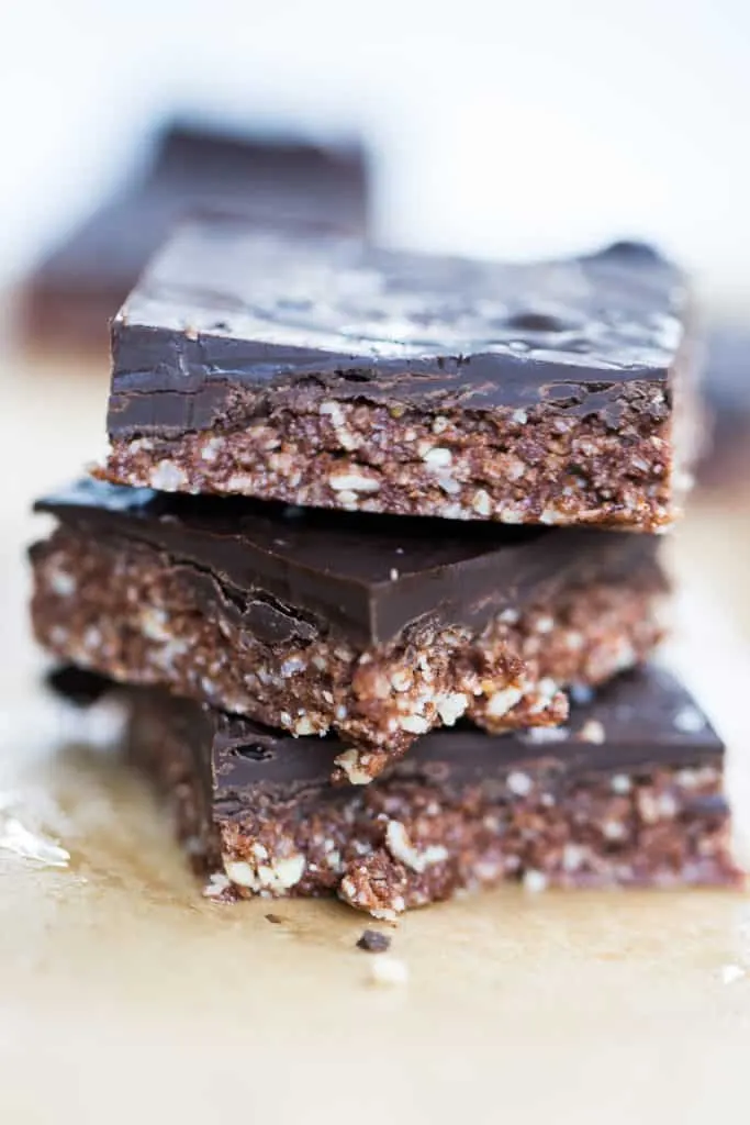 Tres barras de proteína caseras cubiertas de chocolate, apiladas sobre papel de horno